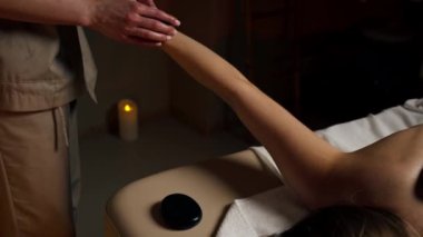 Masaj masasındaki masaj salonunda çıplak sırt masajı yapan siyah taşlı bir kız el masajının özel yerlerine uzanmış.