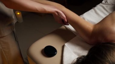 Masaj masasındaki masaj salonunda çıplak sırt masajı yapan siyah taşlı bir kız el masajının özel yerlerine uzanmış.