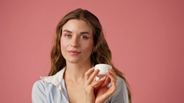 Stüdyonun güzellik çekimini kapat pembe arka planda uzun saçlı kız iç çamaşırı ve mavi gömlekli doğal güzellik kavanozuyla poz ver.