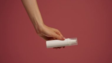 Yakın plan stüdyo güzellik çekimi pembe arka planda kadın elleri uzun beyaz bir kavanoz dolusu yüz kremi güzellik salonu tutuyor.