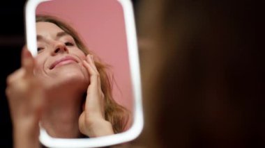 Pembe arka planda bir stüdyonun güzellik çekimi LED ışıklı bir aynaya bakan güzel bir kız cilt değerlendirmesi doğal güzellik kusurlu cilt pozitifliği güzellik salonu