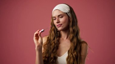Pembe arka planda yakın plan stüdyo. İç çamaşırlı, beyaz saç bandı takan, pembe fırçalı güzel bir kız. Kadın eli ruj sürüyor.