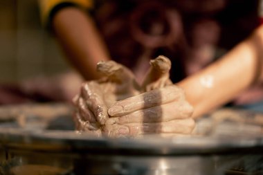 Kil modelleme stüdyosuna yakın genç kız elleri çömlekçi çarkında kil şekillendiriyor eski sanat eserleri öğretmenine yardım ediyor.