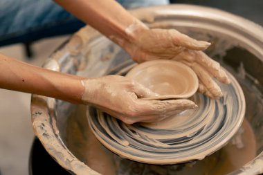 Kil modelleme stüdyosuna yakın genç kız elleri çömlekçi çarkında kil şekillendiriyor eski sanat eserleri öğretmenine yardım ediyor.