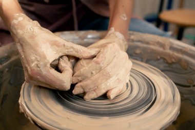 Kil modelleme stüdyosuna yakın genç kız elleri çömlekçi çarkında kil şekillendiriyor eski sanat eserleri öğretmenine yardım ediyor.