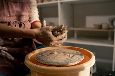 Kil modelleme stüdyosunda genç sarışın bir kız çömlekçi çarklarıyla çalışmayı öğreniyor. Tabakları şekillendiriyor.