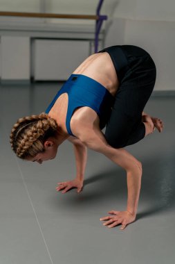 Ruhani gelişim stüdyosunda yoga sınıfında orta yaşlı mavi bluzlu bir kız ve parlak bir odada pantolon giyerek sadece amuda kalkma egzersizi yapar.