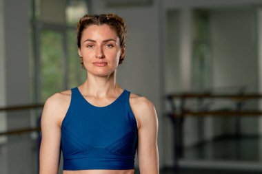 Ruhani gelişim yüksek lisans sınıfında yoga sınıfında orta yaşlı bir kız mavi bluzlu ve pantolonu parlak bir odada kameraya poz veriyor iyi fiziksel zindelik kameraya bakıyor.