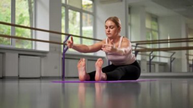 Ruhsal gelişim yüksek lisans sınıfının stüdyosundaki en iyi çekim. Yoga üzerine. Mor bir minderin üzerinde parlak bir odada genç bir kız sırt kasları için esneme hareketi yapıyor.