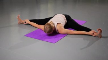Yoga üzerine ruhsal gelişim yüksek sınıfı atölyesinde mor bir minderin üzerinde parlak bir odada genç bir kız sırt germe hareketleri yapıyor.