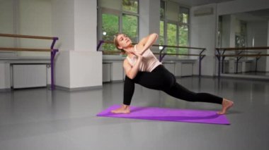 Ruhsal gelişim yüksek lisansı sınıfında yoga sınıfında genç bir kız parlak bir odada mor bir minder üzerinde elleri bağlı ve bacaklarını açmış bir şekilde Asana pozisyonunda.