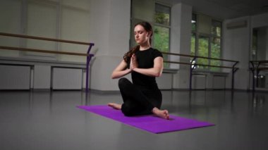 Uzun saçlı, siyah eşofmanlı, mor minderli, kolları ve bacakları katlanmış, Asana pozu veren yoga kızı üzerine ruhsal gelişim yüksek lisans sınıfında.