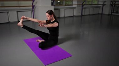 Uzun saçlı, siyah eşofmanlı, uzun saçlı, uzun bacaklı, yoga yüksek lisans sınıfında katlanmış bacaklarıyla oturup Asana pozu veriyor.