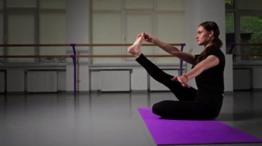 Uzun saçlı, siyah eşofmanlı, uzun saçlı, uzun bacaklı, yoga yüksek lisans sınıfında katlanmış bacaklarıyla oturup Asana pozu veriyor.