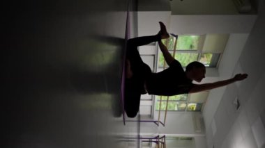 Ruhsal gelişim yüksek lisans sınıfının stüdyosundaki dikey video. Mor minderdeki uzun saçlı yoga kızı. Bacağını geriye çekiyor.