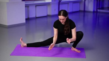 Mor minderli uzun saçlı yoga kızı üzerine ruhsal gelişim yüksek sınıfı atölyesinde uzanan bacağını yana doğru uzatarak Asana pozu veriyor.