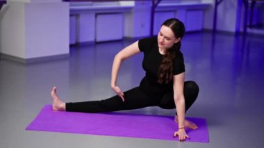 Mor minderli uzun saçlı yoga kızı üzerine ruhsal gelişim yüksek sınıfı atölyesinde uzanan bacağını yana doğru uzatarak Asana pozu veriyor.