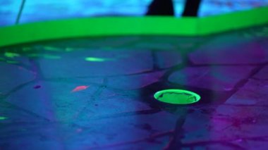 Etekli kız, renkli, kapalı bir mini golf maçında topu delikten çıkarıyor.