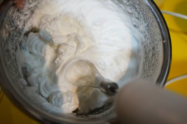 Bir el çırpma makinesine aşırı yakın. Beyaz yumurta kremasını bir kaseye karıştırıyor.