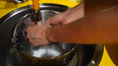 Washing up a cooking bowl under a sink with tap water flowing using a sponge