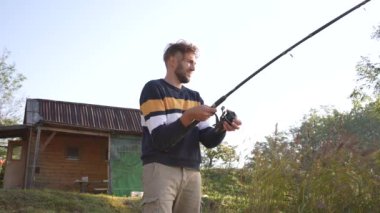 Angler reeling in a fish in front of an old wooden cabin