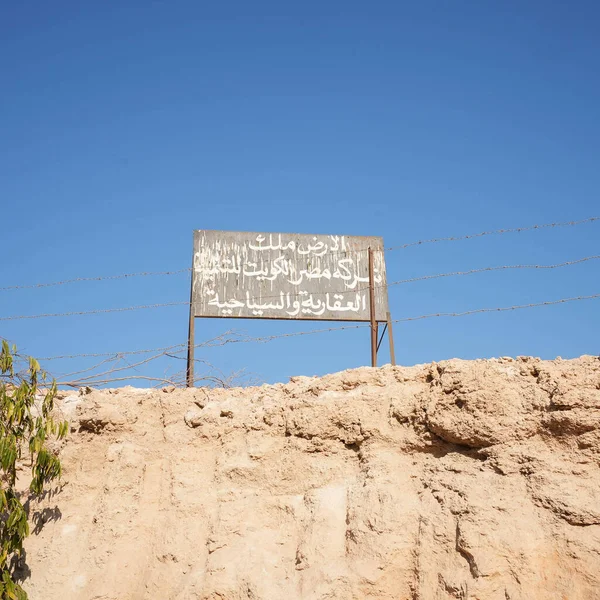 Üzerinde mavi gökyüzü ve ön planda tel örgüler olan Arapça harflerle yazılmış bir tahta. Yüksek kalite fotoğraf