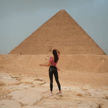 Giza Piramidinin önünde duran deri pantolonlu, uzun boylu, güzel bir kız. Yüksek kalite fotoğraf