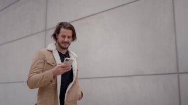 Genç adam şehirde yürürken akıllı telefon kullanırken mutlu bir şekilde gülümsüyor. Boş caddede tek başına dolaşırken hafta sonunun tadını çıkarmakla meşgul bir işadamı.
