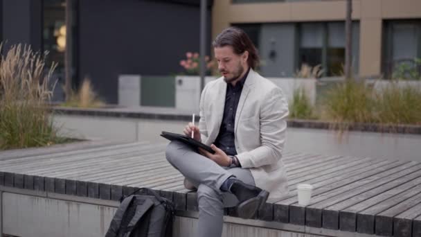 Skoncentrowany Europejski Biznesmen Garniturze Siedzący Ławce Obok Biurowca Korzystający Tabletu — Wideo stockowe