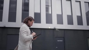 Ofis binasının yanında yürürken Stylus 'u kullanarak tablete yazı yazan profesyonel bir çalışan. Yetişkin girişimci, cihazında kurumsal görevleri çözüyor. Akıllı patron iş stratejisini tartışıyor