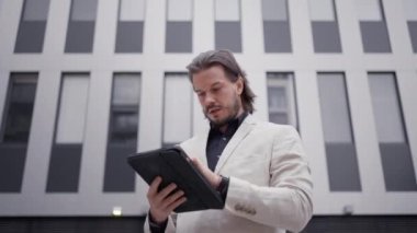 Ofis binasının yanında dururken tablete notlar yazan profesyonel bir çalışan. Yetişkin girişimci iş adamı yeni fikirler üretiyor ve kendi cihazında kurumsal görevler yapıyor. İş stratejisi