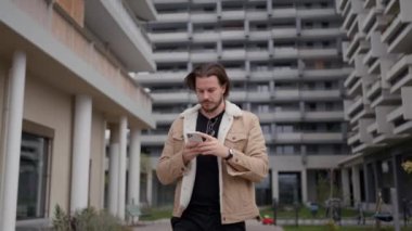 Genç Avrupalı adam sonbahar kentsel caddesinde yürüyor. İş adamı cep telefonu tutuyor, telefon ediyor, konuşuyor. Teknoloji ve insanlar kavramı