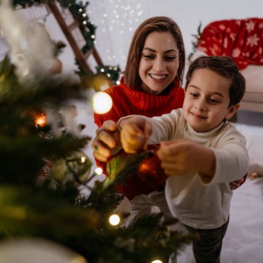 Küçük çocuk annesine Noel ağacı süslemesinde yardım ediyor, dilek diliyor, evde mucizeyi bekliyor. Mutlu Noeller ve mutlu yıllar konsepti