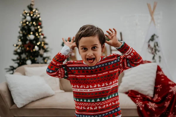 Excited baby looking at the camera and showing funny faces while playing in the living room at home before the Christmas. Happy childhood concept