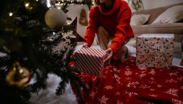 Sıcak bir akşamda Noel ağacının altına hediye koyan kimliği belirsiz kadının yakın görüntüsü. Kış tatili, kutlama ve insanların konsepti