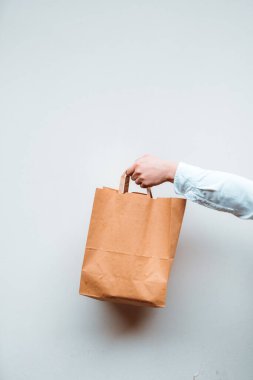 Vertical view of the unknown millennial woman holding paper bag with takeaway food on white background. Food to go concept. Empty space
