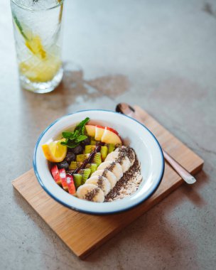 Smoothie bowl with chia seeds, muesli, kiwi, banana slices and flakes standing at the table at the cafe or at home. Stock photo