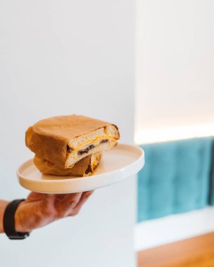 Unknown man hand holding fresh fried sandwich on white plate in restaurant, selective focus. Healthy easy breakfast ideas concept
