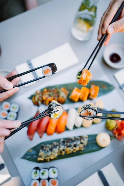  friends hands holding sushi and rolls with wooden chopsticks in the restaurant. Japanese and Chinese cuisine concep