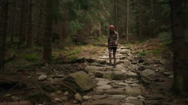 Pretty caucasian woman walking in woods, stepping through stoned path, enjoys the beauty of nature. Hiking, hobby, relaxation, recreation time concept