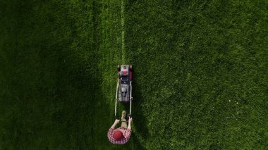 Top view of the lawn-mover worker cutting green grass garden. Unknown man worker cutting grass with lawn mower above view