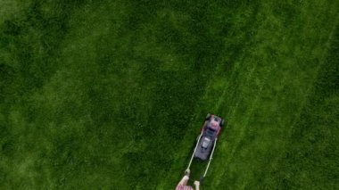 Aerial top view of man mowing grass on football stadium or lawn. Unknown man gardener cuts the grass. Garden care concept