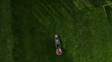 Top view of the lawn mower mows fresh, green grass on the lawn. Municipal worker in uniform with a lawn mower in his hand. Lawn care service concept