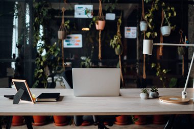 Wooden table with computer laptop, frame, lamp with sun light shine through the window. No people. Beautiful workspace - online work from office concept
