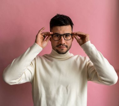 Portrait of bearded man trying on eyeglasses and looking camera attentively while posing isolated over pink background. People emotions concept