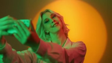 Image of young blonde woman with short hair smiling and taking selfie photo on cellphone isolated over orange background