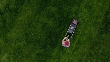 Top view of the lawn-mover worker cutting green grass garden. Unknown man worker cutting grass with lawn mower above view