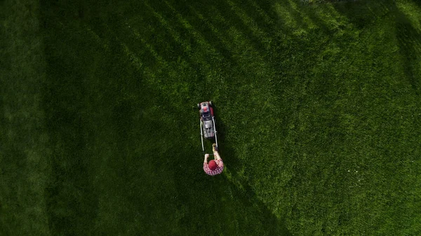 stock image Professional worker with lawn mower mows the grass, top view. Unknown man in work uniform cuts grass alone. Lawn care service concept