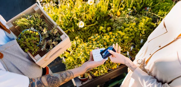 Kvinnen Blomsterbutikken Betaler Med Smarttelefon Pengeoverføring Mobilbetaling Bilde Høy Kvalitet stockbilde