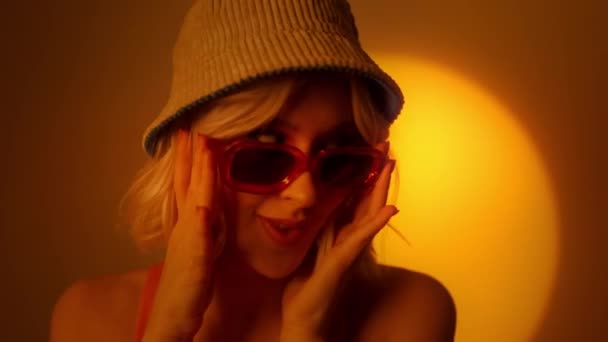 オレンジを背景に流行のサングラスをかけ ライトナチュラルメイクでスタイリッシュな女性モデル グラマラス女性ポルノのスタジオ — ストック動画